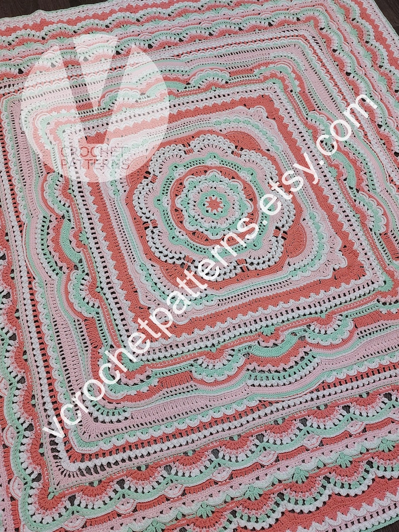 K&ouml;nnte beinhalten: Eine geh&auml;kelte Decke mit einem quadratischen Design in der Mitte. Die Decke ist in verschiedenen Farben gehalten, darunter Rosa, Gr&uuml;n und Wei&szlig;. Die Decke hat einen gewellten Rand.
