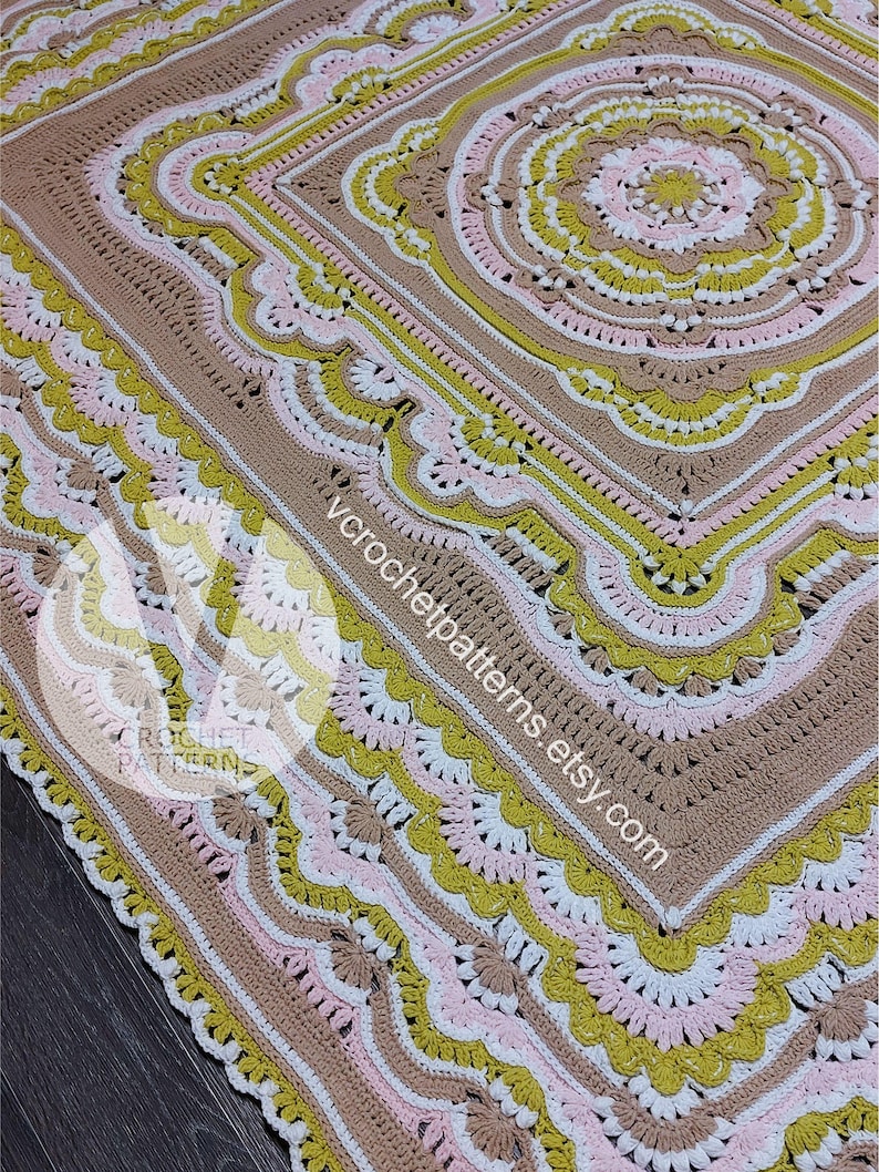 Pode incluir: Uma manta de croch&ecirc; com um padr&atilde;o circular no centro. A manta &eacute; feita com fio marrom, branco, rosa e verde. A manta tem uma borda festonada.