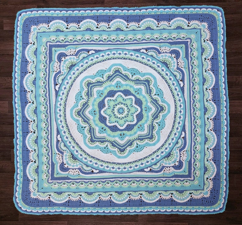 May include: A square, crocheted blanket in shades of blue, teal, and white. The design features concentric circles and squares with intricate patterns, including scalloped edges and floral motifs. The blanket is a handmade textile.