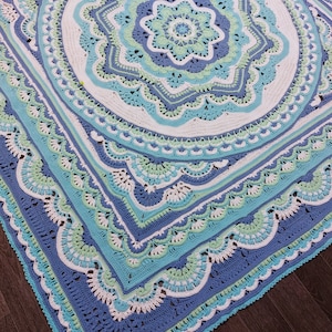 May include: A large, square, crocheted blanket in shades of blue, teal, and white. The intricate design features a central floral motif surrounded by concentric circles and scalloped edges. The blanket is made of soft yarn and is perfect for a bed or sofa.