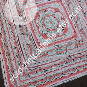 K&ouml;nnte beinhalten: Eine geh&auml;kelte Decke mit einem quadratischen Design in Rosa-, Gr&uuml;n- und Wei&szlig;t&ouml;nen. Die Decke hat einen gewellten Rand und ein zentrales Motiv mit mehreren Schichten komplizierter H&auml;kelmaschen.