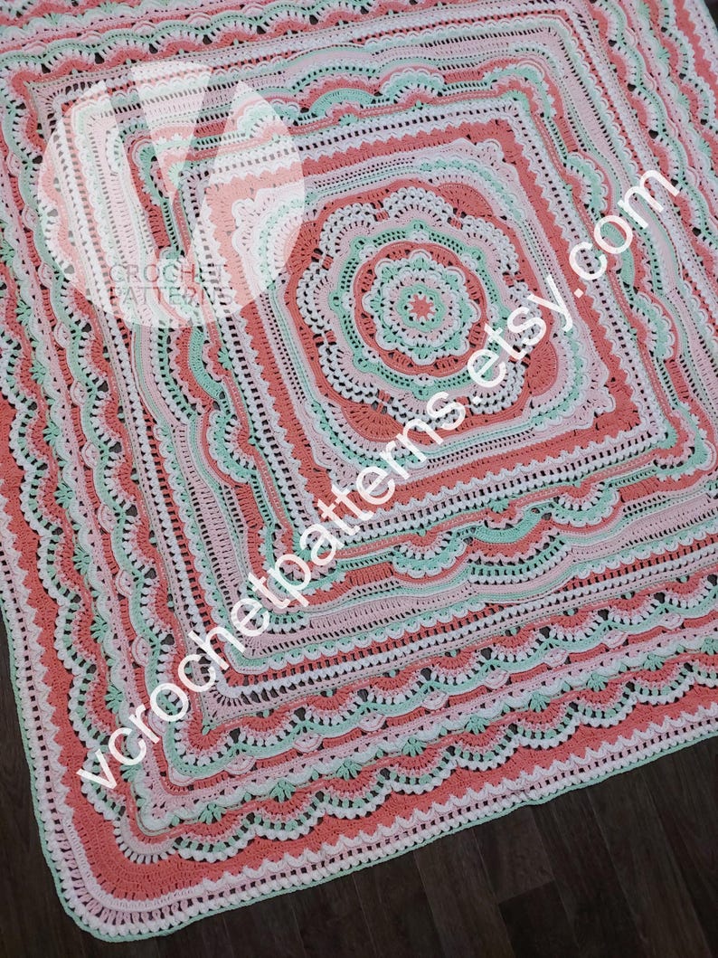 K&ouml;nnte beinhalten: Eine geh&auml;kelte Decke mit einem quadratischen Design in Rosa-, Gr&uuml;n- und Wei&szlig;t&ouml;nen. Die Decke hat einen gewellten Rand und ein zentrales Motiv mit mehreren Schichten komplizierter H&auml;kelmaschen.