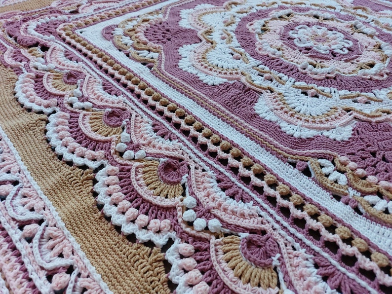 Peut inclure: Une couverture au crochet avec un motif rose, blanc et marron. La couverture pr&eacute;sente un design d&eacute;taill&eacute; et complexe avec un m&eacute;daillon central et une bordure de bords festonn&eacute;s.