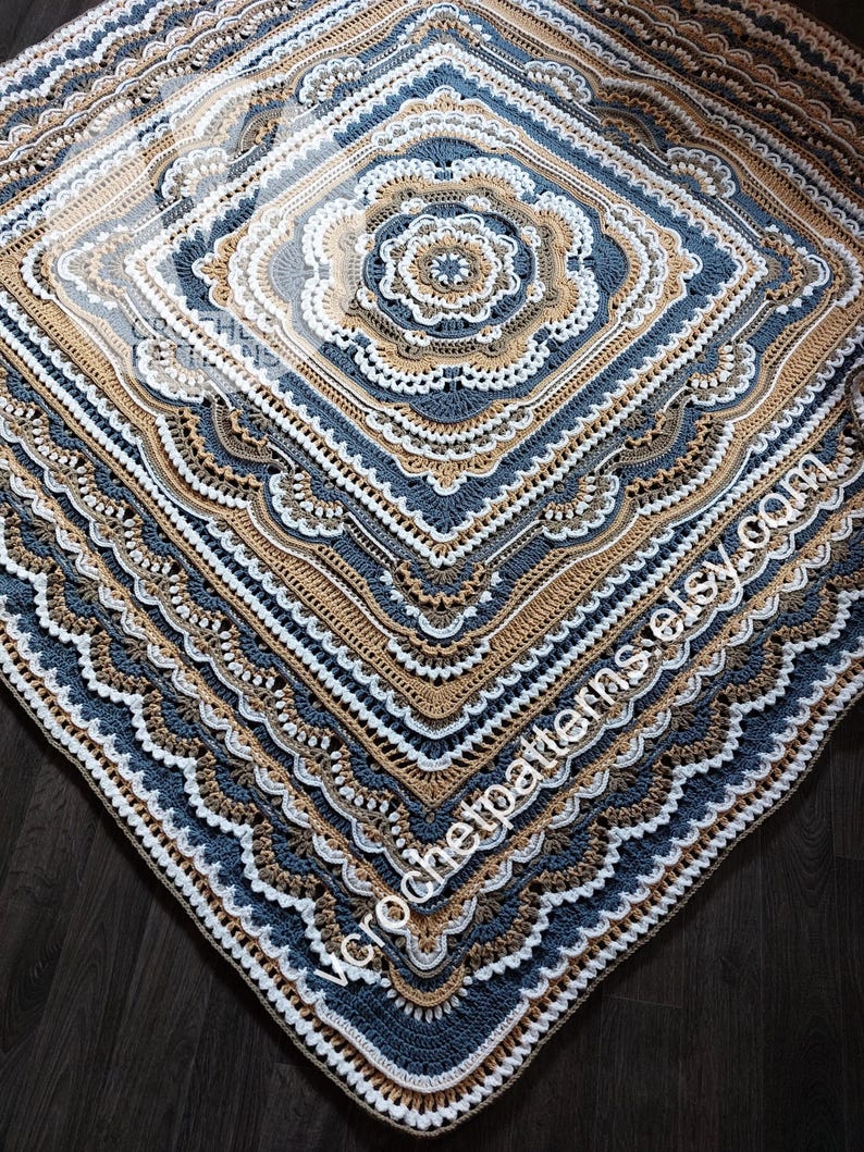 K&ouml;nnte beinhalten: Eine geh&auml;kelte Decke mit einem quadratischen Muster in Blaut&ouml;nen, Braun und Wei&szlig;. Die Decke hat einen detaillierten Rand mit mehreren Schichten geh&auml;kelter Maschen.