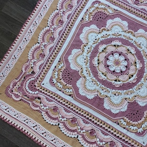 Peut inclure: Une couverture au crochet avec un grand motif de mandala complexe dans des tons de rose, blanc et beige. La couverture est de forme carr&eacute;e avec une bordure festonn&eacute;e.