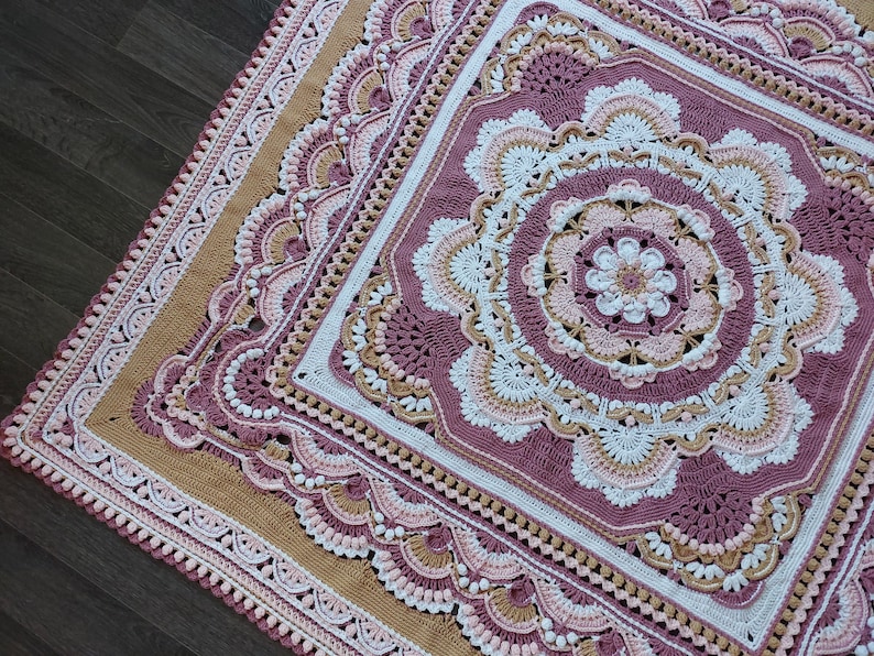 Peut inclure: Une couverture au crochet avec un grand motif de mandala complexe dans des tons de rose, blanc et beige. La couverture est de forme carr&eacute;e avec une bordure festonn&eacute;e.