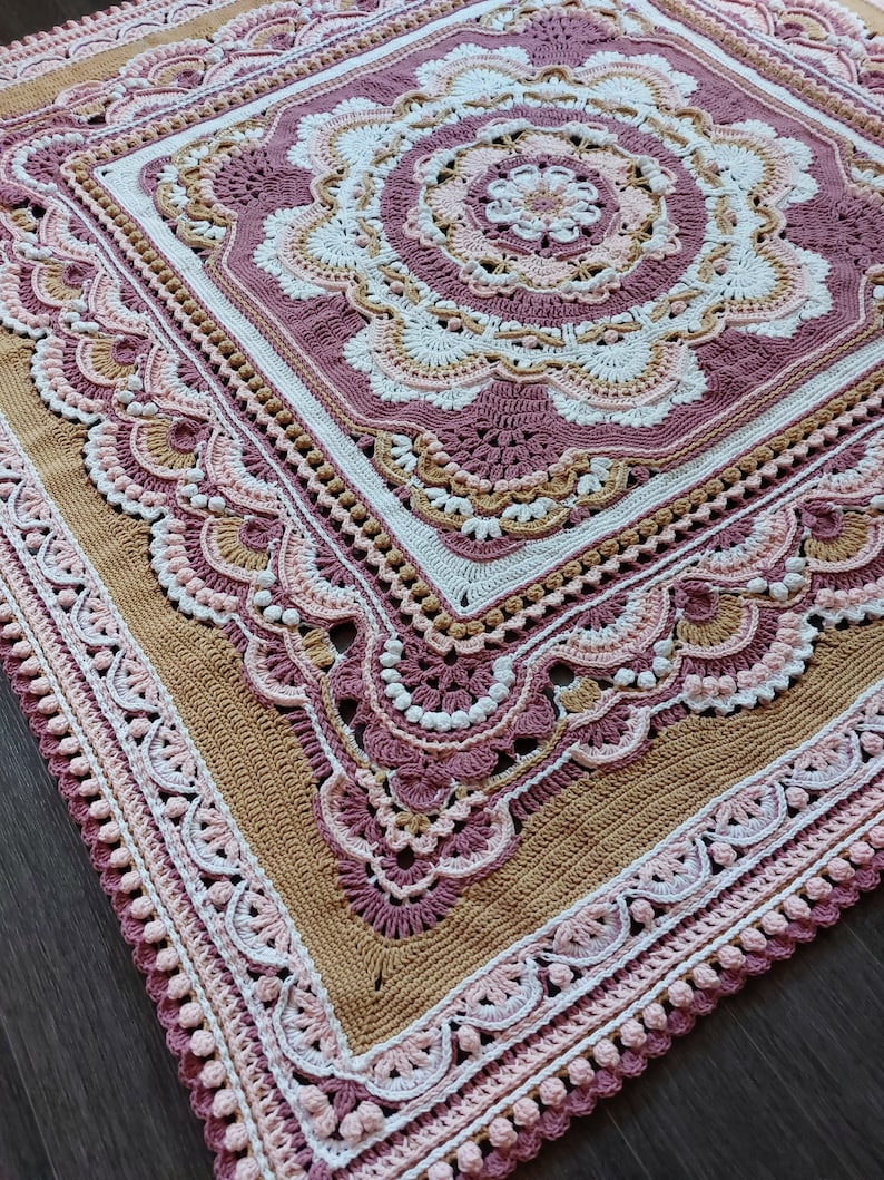 Peut inclure: Une couverture au crochet avec un grand motif floral complexe dans des tons de rose, blanc et beige. La couverture est de forme carr&eacute;e et a une bordure d&eacute;licate.