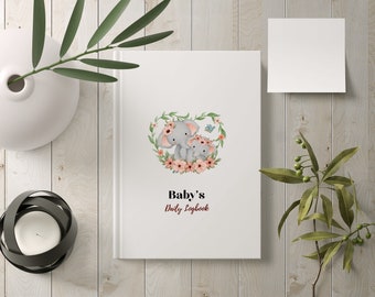 May include: A white journal with a floral heart design featuring two gray elephants. The text "Baby's Daily Logbook" is printed below the elephants.