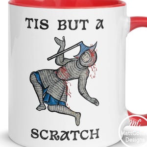 Könnte beinhalten: Weißer Keramikbecher mit rotem Innenraum und Griff. Der Becher zeigt den Text "TIS BUT a SCRATCH" mit einer Illustration eines mittelalterlichen Ritters. Der Ritter ist mit einer Streitaxt dargestellt und scheint verletzt zu sein.