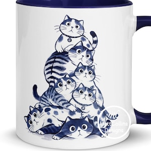 May include: White ceramic mug with a navy blue interior and handle. The mug features a whimsical illustration of several blue and white cats stacked on top of each other. The design includes a variety of cat poses and patterns.