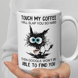 Op de afbeelding: Een witte keramische koffiemok met een zwart-witte illustratie van een kat die een kopje koffie vasthoudt. De tekst op de mok luidt "Touch my coffee I will slap you so hard even Google won't be able to find you."