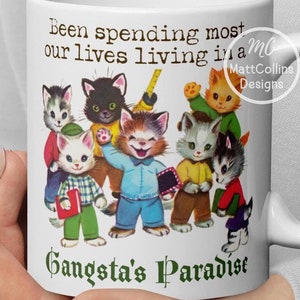 May include: White ceramic mug featuring a group of cartoon cats with the text "Been spending most our lives living in a Gangsta's Paradise." The mug has a white handle and a design by Matt Collins Designs.