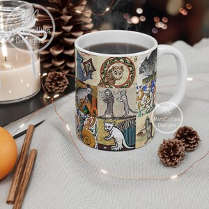 May include: White ceramic mug featuring a collage of medieval-style illustrations of cats and other creatures. The mug has a white handle and is filled with a dark liquid. The design includes an owl, cats reading books, and other whimsical figures.
