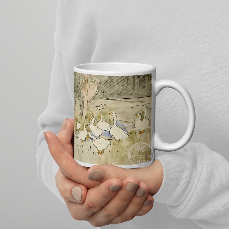 May include: White ceramic mug with a watercolor illustration of a group of geese in a pond setting. The illustration is in shades of brown, gray, and blue. The mug has a black handle and the text "Matt Callina Designs" is printed on the bottom.
