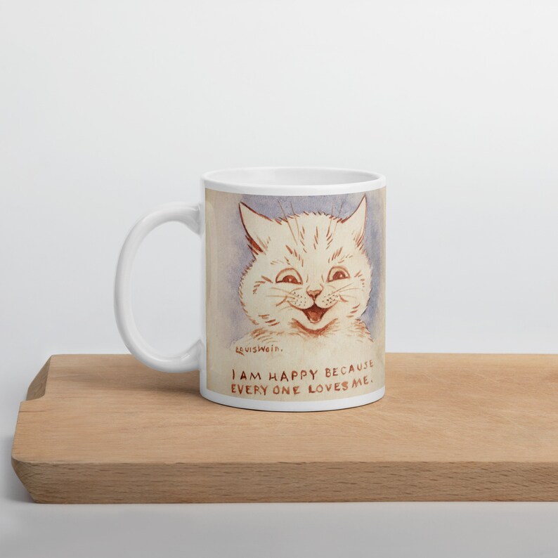 Pu&ograve; includere: Tazza in ceramica bianca con un'illustrazione di un gatto sorridente e il testo "Sono felice perch&eacute; tutti mi amano."