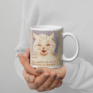 Pu&ograve; includere: Tazza in ceramica bianca con un'illustrazione di un gatto bianco con un grande sorriso. Il testo sulla tazza recita "Sono felice perch&eacute; tutti mi amano."