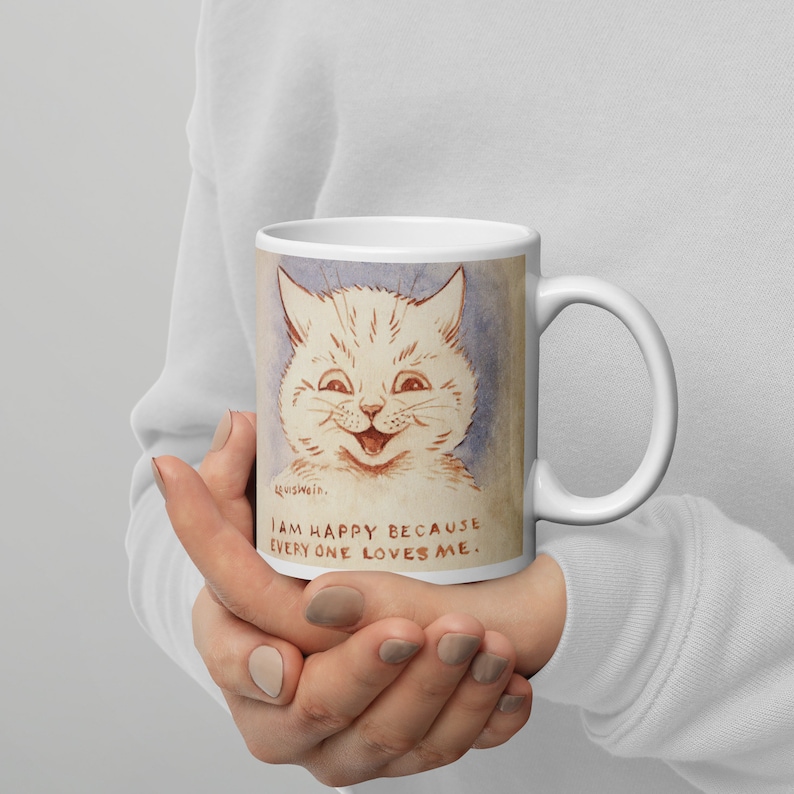 Pu&ograve; includere: Tazza in ceramica bianca con un'illustrazione di un gatto bianco con un grande sorriso. Il testo sulla tazza recita "Sono felice perch&eacute; tutti mi amano."