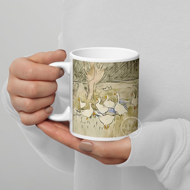 May include: White ceramic mug with a hand-drawn illustration of a group of white geese in a field. The geese are facing different directions and some are in the water. The background is a light brown color with a dark brown tree in the background. The mug has a black handle and the text "Matt Collin Designs" is printed on the bottom right corner.