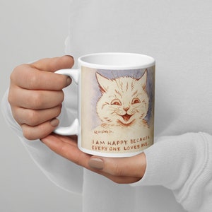 Pu&ograve; includere: Tazza in ceramica bianca con un'illustrazione di un gatto sorridente con il testo "Sono felice perch&eacute; tutti mi amano."