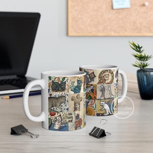 May include: White ceramic coffee mug featuring a collage of medieval cat illustrations in various poses and settings. The artwork includes cats in crowns, armor, and other whimsical scenes. The mug has a curved handle and a glossy finish.