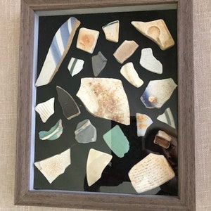 May include: A framed display of various ceramic shards and fragments, showcasing a collection of broken pottery pieces in a variety of colours and patterns.