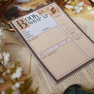 Può includere: Un blocco note marrone e beige per riassunti di libri con sezioni per titolo, autore, genere e recensione. Il blocco note ha un bordo decorativo e le parole "Book Wrap Up" in alto. Il blocco note è sopra pagine di vecchi libri.