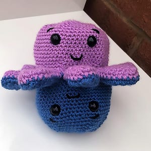 Op de afbeelding: Een gehaakt octopus knuffel met een paarse kop en een blauw lichaam. De octopus heeft zwarte ogen en een glimlachende mond.