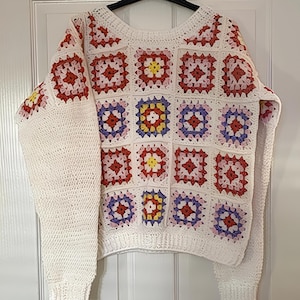 May include: White crochet sweater with a colorful granny square pattern in shades of pink, purple, red, and yellow.
