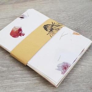 May include: A stack of blank note cards with floral designs printed on them. The cards are wrapped in brown paper and tied with a string.