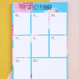 May include: A weekly planner with a blue background and pink floral design. The planner has spaces for each day of the week, Monday through Sunday, and a notes section.