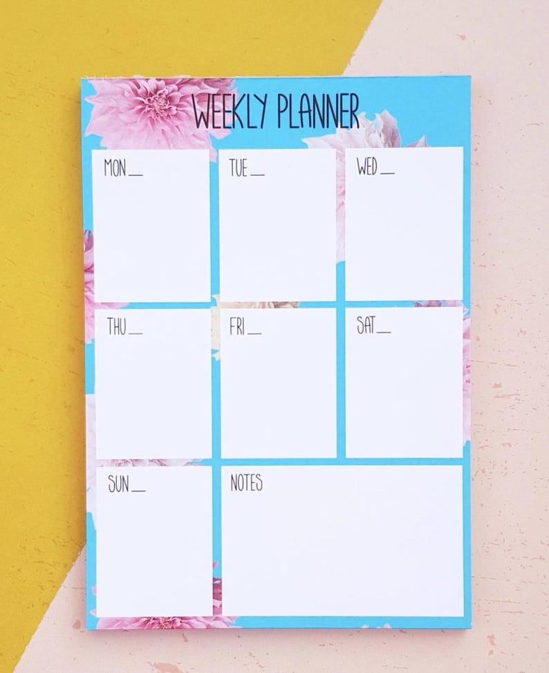 May include: A weekly planner with a blue background and pink floral design. The planner has spaces for each day of the week, Monday through Sunday, and a notes section.