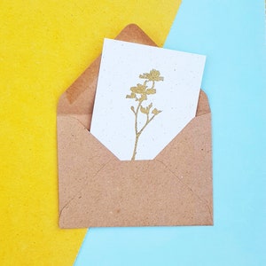 May include: A brown paper envelope with a white card inside. The card has a gold silhouette of a flower on it.