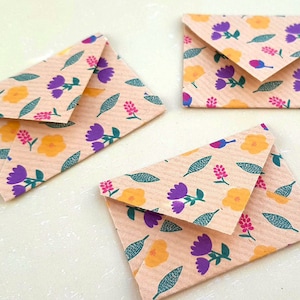 Peut inclure: Trois petites enveloppes avec un motif floral. Les enveloppes sont beiges avec des fleurs violettes, jaunes et vertes.