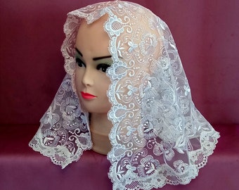 May include: White lace mantilla with floral embroidery. The mantilla is a traditional head covering worn by women.