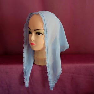 May include: A light blue sheer headscarf with a white lace trim. The scarf is folded in a triangular shape and is worn on a mannequin's head.