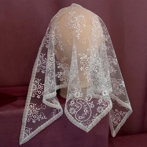 Puede incluir: Velo de encaje blanco con un patrón floral. El velo está adornado con un delicado borde de encaje.