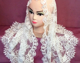 May include: White lace mantilla with a scalloped edge. The lace is delicate and intricate, with a floral pattern. The mantilla is draped over a mannequin's head.