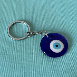 May include: A silver key chain with a blue evil eye charm. The charm has a white center with a blue pupil and a black dot in the center.