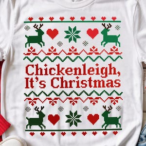 Könnte beinhalten: Weißes T-Shirt mit weihnachtlichem Design. Das Shirt zeigt ein Muster aus grünen Rentieren, roten Herzen und Schneeflocken mit dem Text "Chickenleigh, It's Christmas" in Rot. Das T-Shirt wird mit blauen Jeans und weißen Turnschuhen kombiniert.
