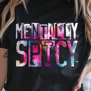 Puede incluir: Camiseta negra con el texto "MENTALLY SPICY" en un dise&ntilde;o colorido estilo acuarela. La camiseta se combina con shorts vaqueros grises. El conjunto es informal y elegante.