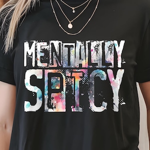 Puede incluir: Camiseta negra con la frase "MENTALLY SPICY" en blanco. La palabra "SPICY" presenta un efecto tie-dye colorido. Una prenda casual y moderna.