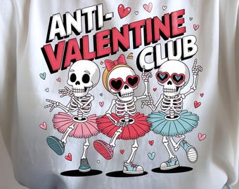 May include: White t-shirt with the text "ANTI-VALENTINE CLUB" and a graphic of three dancing skeletons wearing tutus and heart-shaped sunglasses. The skeletons are in pink, red, and blue tutus.