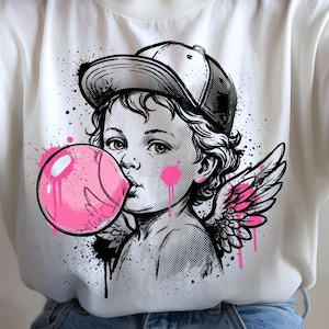 May include: White t-shirt featuring a black and white graphic of a cherub blowing a pink bubblegum bubble. The cherub wears a baseball cap and has pink wings. The design includes pink and black paint splatter.