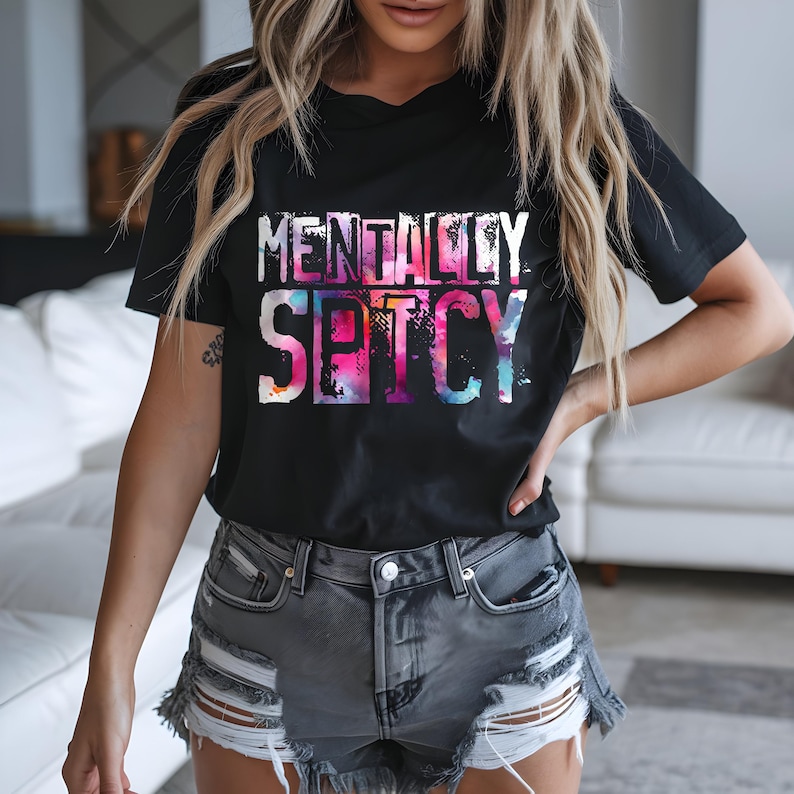 Puede incluir: Camiseta negra con el texto "MENTALLY SPICY" en un dise&ntilde;o colorido estilo acuarela. La camiseta se combina con shorts vaqueros grises. El conjunto es informal y elegante.