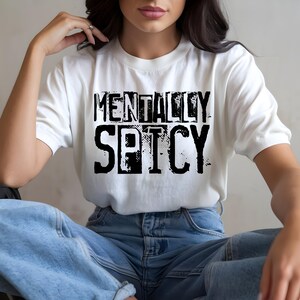 Puede incluir: Camiseta blanca con el texto "MENTALLY SPICY" en negrita, negro y con un dise&ntilde;o desgastado. La camiseta se combina con vaqueros azules. El estilo es informal y c&oacute;modo.