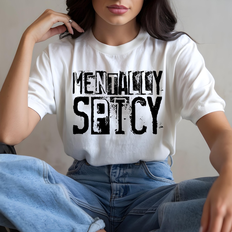 Puede incluir: Camiseta blanca con el texto "MENTALLY SPICY" en negrita, negro y con un dise&ntilde;o desgastado. La camiseta se combina con vaqueros azules. El estilo es informal y c&oacute;modo.