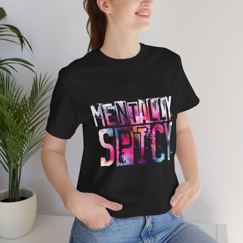 Puede incluir: Camiseta negra con el texto "MENTALLY SPICY" en un dise&ntilde;o colorido estilo acuarela. El texto es blanco con una vibrante mezcla de tonos rosas, morados y azules. La camiseta es de cuello redondo.