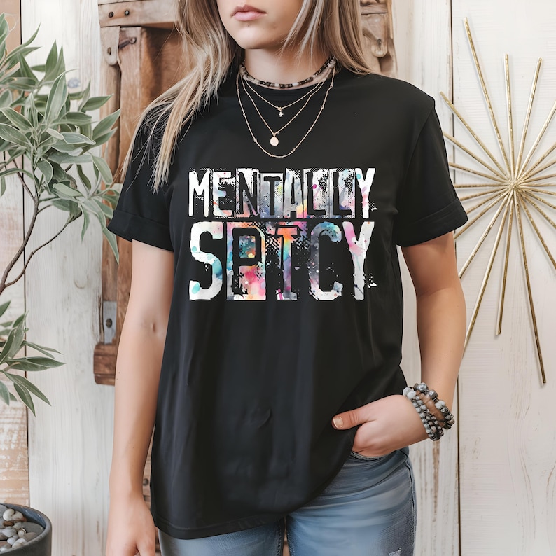 Puede incluir: Camiseta negra con la frase "MENTALLY SPICY" en blanco. La palabra "SPICY" presenta un efecto tie-dye colorido. Una prenda casual y moderna.