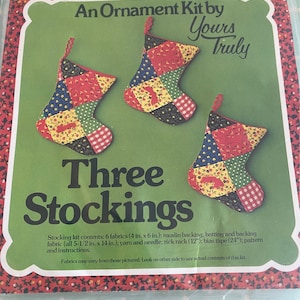 May include: A craft kit to make three patchwork Christmas stockings. The kit includes six 4 x 6 inch fabric squares, muslin backing, batting, yarn, a needle, rick rack, bias tape, and instructions.  "An Ornament Kit by Yours Truly" and "Three Stockings" are printed on the front of the package.