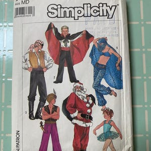 May include: A Simplicity sewing pattern envelope, size MD, featuring illustrations of six costumes: a pirate, a vampire with a red-lined cape, a belly dancer, a genie, Santa Claus with a sack, and a ballerina in a light blue tutu.
